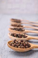 Spoons with peppercorns on grey wooden table, closeup