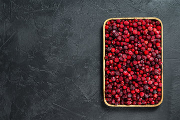 Frozen cranberries in a wooden bowl. Black background. Top view. Space for text