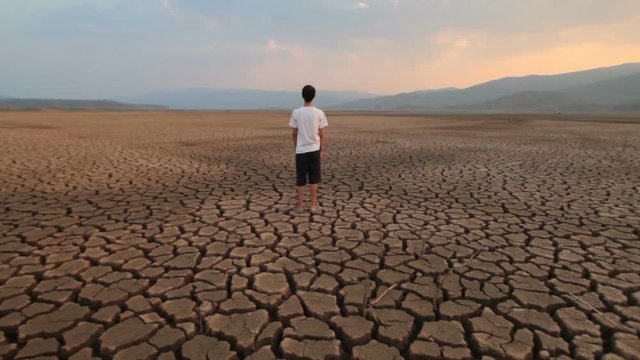 Children and Climate change. Asian Young man standing at middle dry lake metaphor Water crisis, Drought and Global warming
