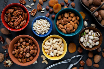 Variety of different types of nuts - almonds, pine nuts, pastachio, cashew, pecan and hazelnuts- in bowls. Overhead view