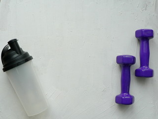 Obraz na płótnie Canvas Two purple dumbbells and sports water bottle on a white textured background with space for your text.