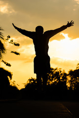 Silhouette Young man happily jumping against sunset sky.