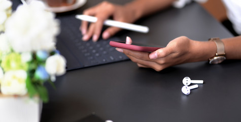 Close-up view of young businesswoman typing on digital tablet while using  smartphone