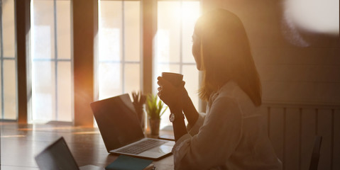 Cropped shot of young businesswoman working with laptop computer and drinking a cup of coffee