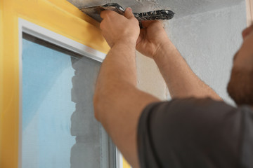 Man plastering window area with putty knife indoors, closeup. Interior repair