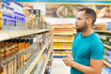 Focused African American man choosing alcohol drinks. Serious bearded guy standing in aisle and looking at drinks. Shopping concept