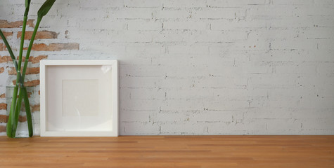 Cropped shot of vintage workplace with mock up frame and copy space on wooden table and brick wall