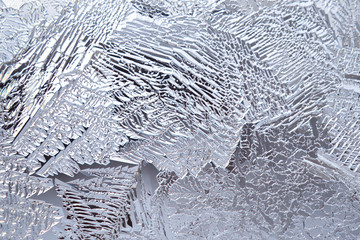 Ice and frost on a window pane in winter. Pattern from the leaves of fantastic plants. Crystals of frozen water close-up. Weather forecast: cold, frost, cooling. Abstract light background or wallpaper