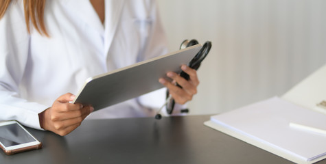 Cropped shot of young female doctor reading medical charts with tablet