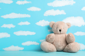 Teddy bear on wooden table near wall with painted blue sky, space for text. Baby room interior