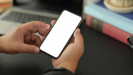 Close-up view of young businessman using blank screen smartphone in dark modern office