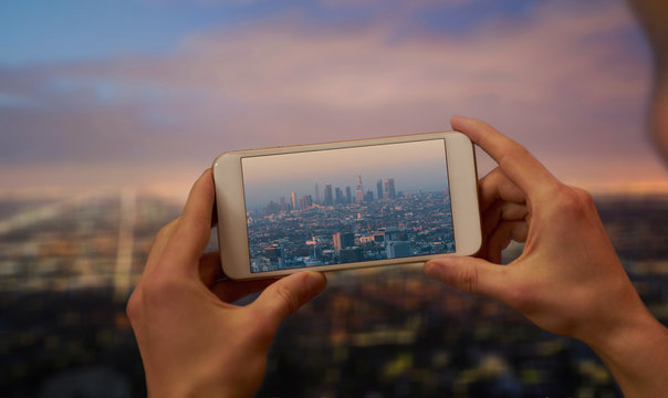 Hands holding a mobile phone and taking a picture of skyscrapers in Los Angeles at dusk
