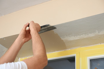 Man plastering window area with putty knife indoors, closeup. Interior repair