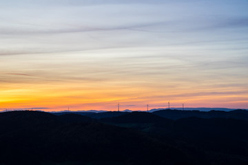 Germany, Orange sunset sky over silhouette of many wind engines in mountainous black forest nature landscape as a symbol for future energy production