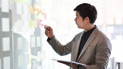 Young passionate businessman collecting the ideas from sticky note in modern office