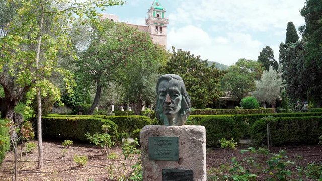 Static view of a head statue of Fr&eacute;d&eacute;ric Chopin in town of Valdemossa in Mallorca island in Spain with green bushes, church and people in the background.