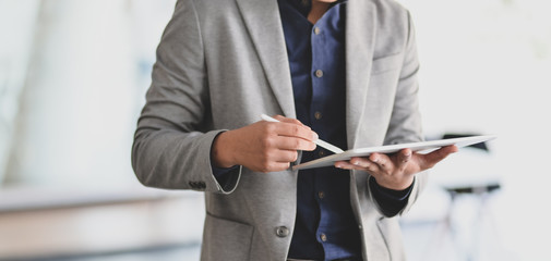 Cropped shot of young businessman working on his project while using digital tablet in modern office