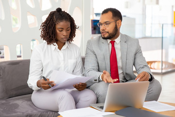 Serious business people discussing contract. Focused African American businessman and businesswoman working with papers and using laptop computer in office. Cooperation concept