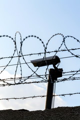 Security camera behind barbed wire fence on the wall, prison, security, crime or illegal...