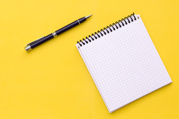 Notebook with a spiral and pen lie on a yellow background, flat lay
