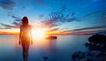 Silhouette of slim sexy girl standing on a beach with sunset