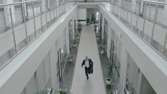 Businessman in formal suit running through office hall atrium of business center. Office worker is late for work and hurrying to meeting with briefcase in hand