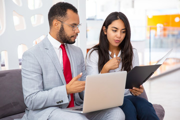 Fototapeta premium Coworkers with folder and laptop discussing work. Professional multiethnic businessman and businesswoman working with laptop computer and documents in office. Cooperation concept
