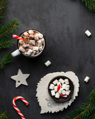 Obraz na płótnie Canvas Hot chocolate with marshmallows and cocoa powder, candy canes, white star and fir tree branches on dark black textured background