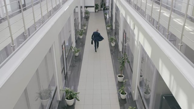 Businessman in formal suit running through office hall atrium of business center. Office worker is late for work and hurrying to meeting with briefcase in hand