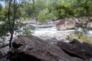 Fototapeta premium Waterfall with a strong flood of water rocks below. Crystal clear water, huge stones with a beautiful vegetation around.At the end forming a strong current and later a calm lake with clean transparent