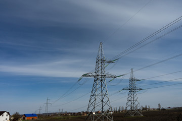 High voltage lines and power pylons on a sunny day with cirrus clouds in the blue sky.