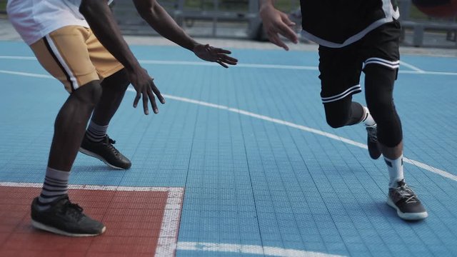 Close Up of Two Young Active Mixed Race Mens Legs Playing Basketball, Bouncing and Throwing ball, One on One at the Street Sports Basketball Court. Healthy Lifestyle and Sport Concept.
