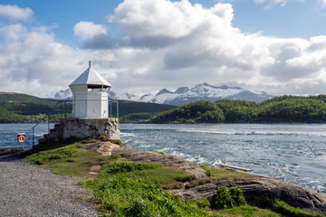 Fototapeta na wymiar Saltstraumen river in Bodo in Northern Norway. Snow covered mountains in the background and blue cloudy sky, lighthouse in the foreground. Traveling and holiday concept.