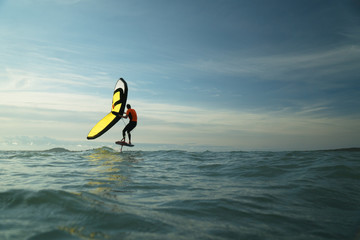 Man riding a hydrofoil surfboard using a hand held foil wing.