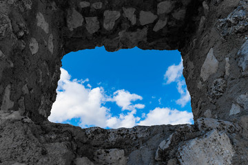 Window on ancient stone wall overlooking a blue sky with clouds