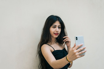 Naklejka premium One Indian female outdoor taking selfie with smart mobile phone on isolated background