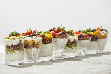 selective focus of delicious granola in glasses with fruits and berries on grey concrete surface isolated on white