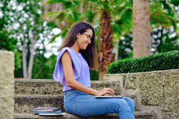 Smiling student girl preparing for exams outdoors with computer