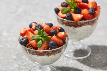 selective focus of delicious granola with berries and yogurt with chia seeds on grey concrete surface