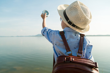 Back view of the boy holding a compass by the lake summer vacation concept.