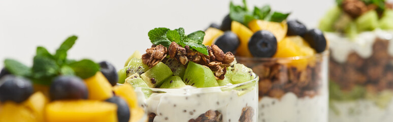 selective focus of fresh granola with kiwi and canned peach with blueberries isolated on white, panoramic shot