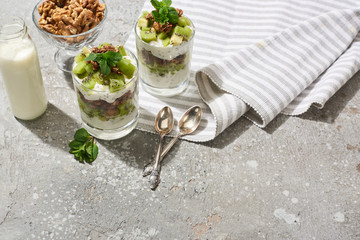 fresh granola with kiwi and yogurt on grey concrete surface with striped napkin, bottle of milk,...