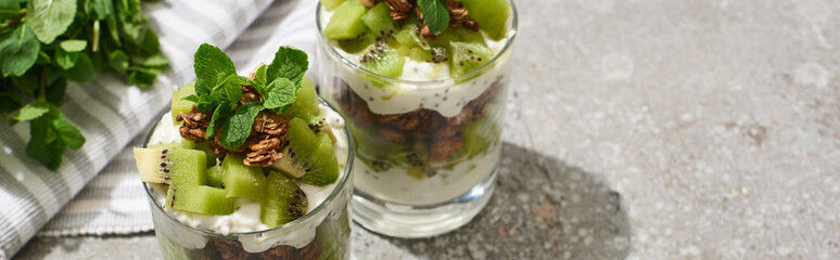fresh granola with kiwi and yogurt on grey concrete surface with striped napkin and mint, panoramic shot