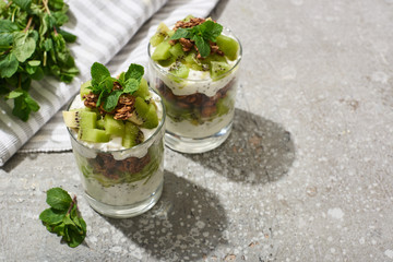 fresh granola with kiwi and yogurt on grey concrete surface with striped napkin and mint