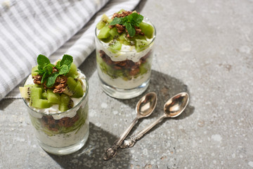 fresh granola with kiwi and yogurt on grey concrete surface with striped napkin, spoons