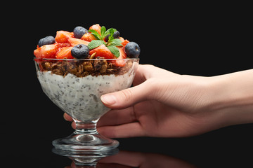 cropped view of woman holding glass with fresh granola with berries and chia seeds isolated on black