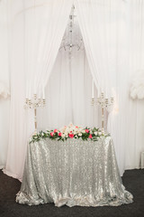 Festive table with a silver tablecloth of sequins, two candelabra with candles, a composition of flowers. Wedding decor