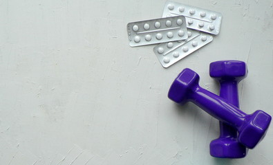 Two purple dumbbells and pills on a white textured background with space for your text.