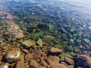 Pebbles covered with moss in crystal clear water.