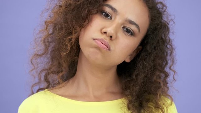 Close up view of attractive african young woman in yellow t-shirt feeling tired and rolling her eyes while looking at the camera  over purple background isolated 